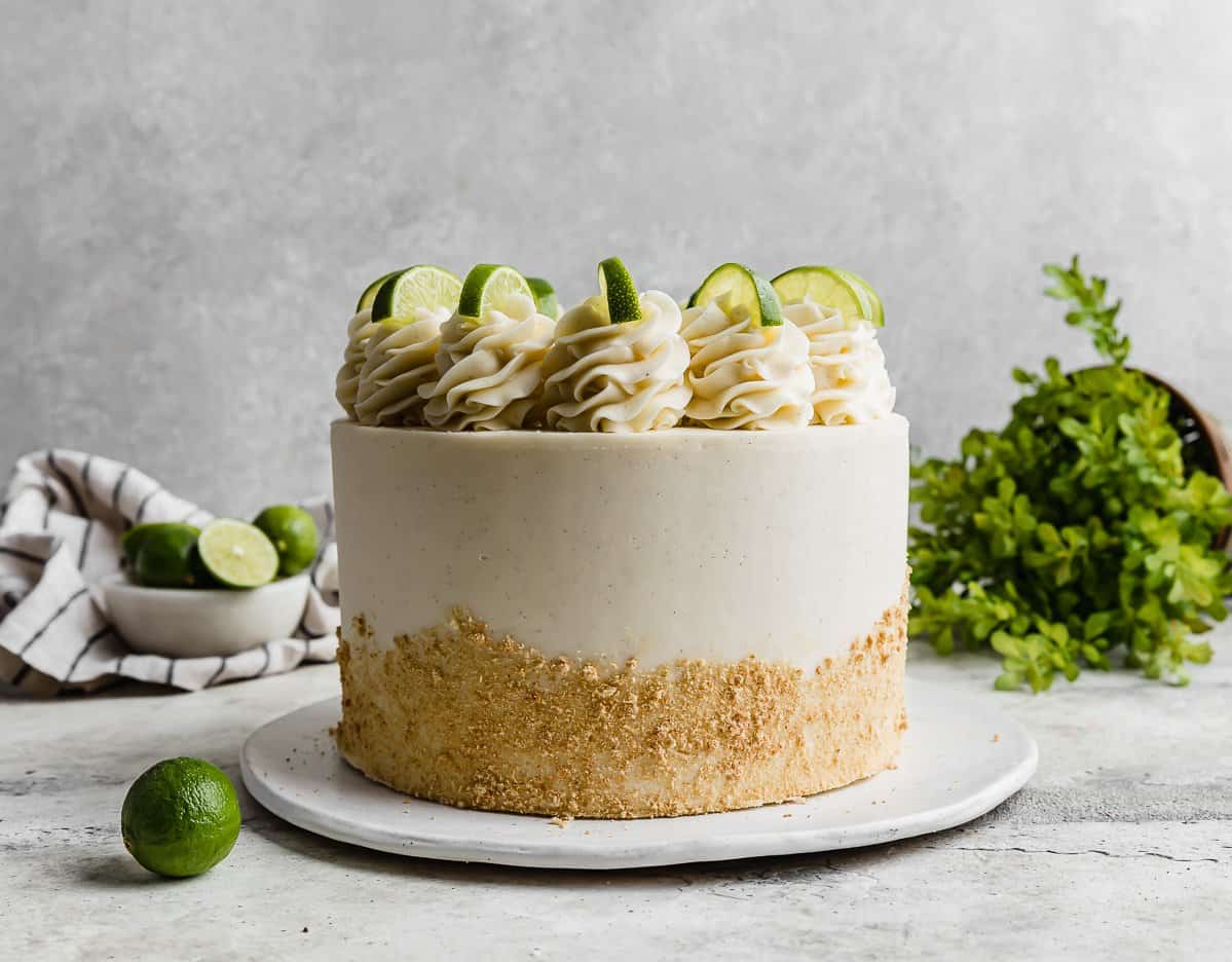 A Key Lime Cake topped with frosting swirls and lime slices against a light grey background.