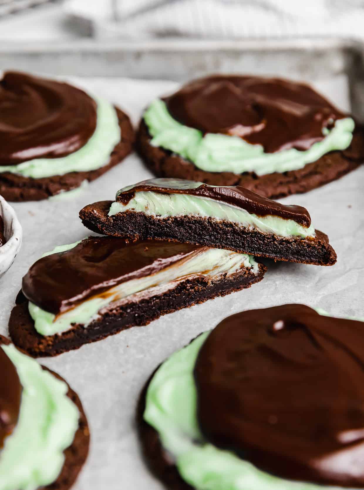 A Copycat Crumbl Mint Brownie Cookie cut in half on a white parchment paper. 
