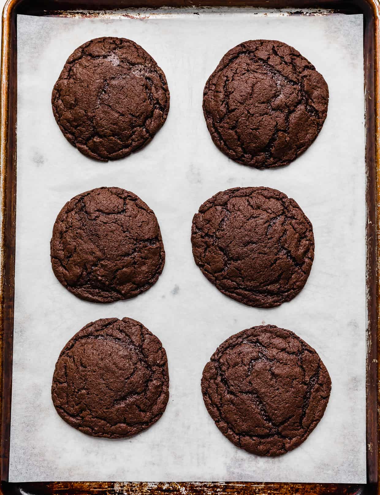 Six baked chocolate cookies on a white parchment paper.