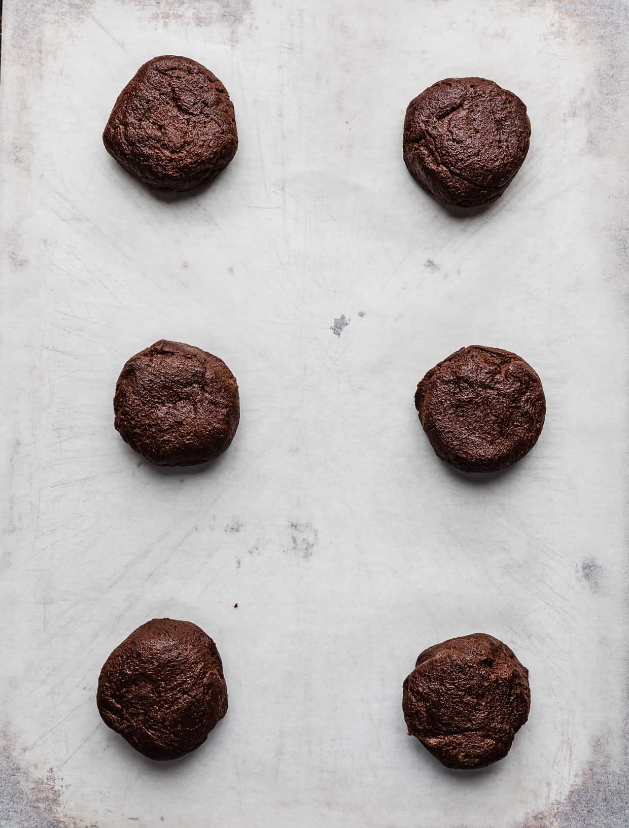 Six chocolate cookie dough balls on a white parchment paper.