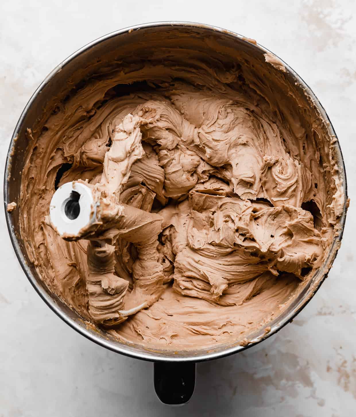A light brown colored butterscotch chocolate buttercream frosting in a metal mixing bowl used to frost a Scotcheroo Cake.