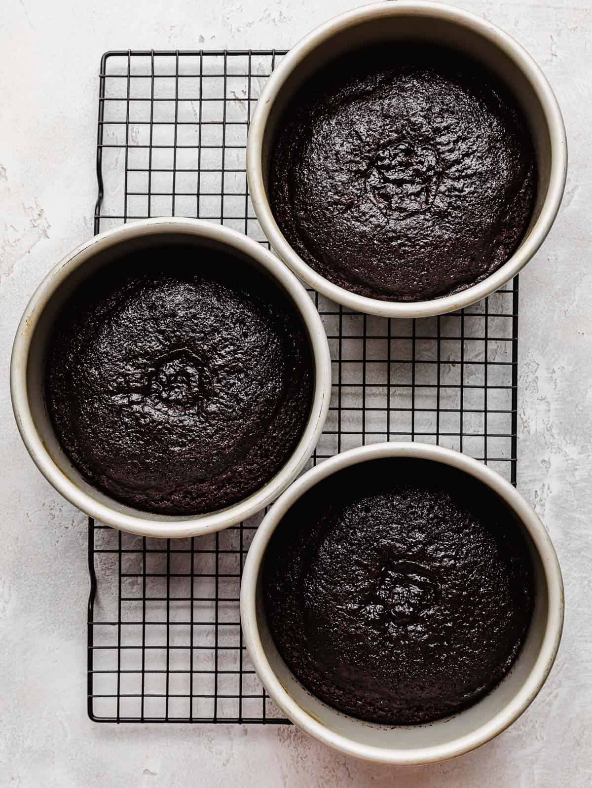Three six inch round cake pans with baked German chcoolate cake layers in each pan on a wire rack.