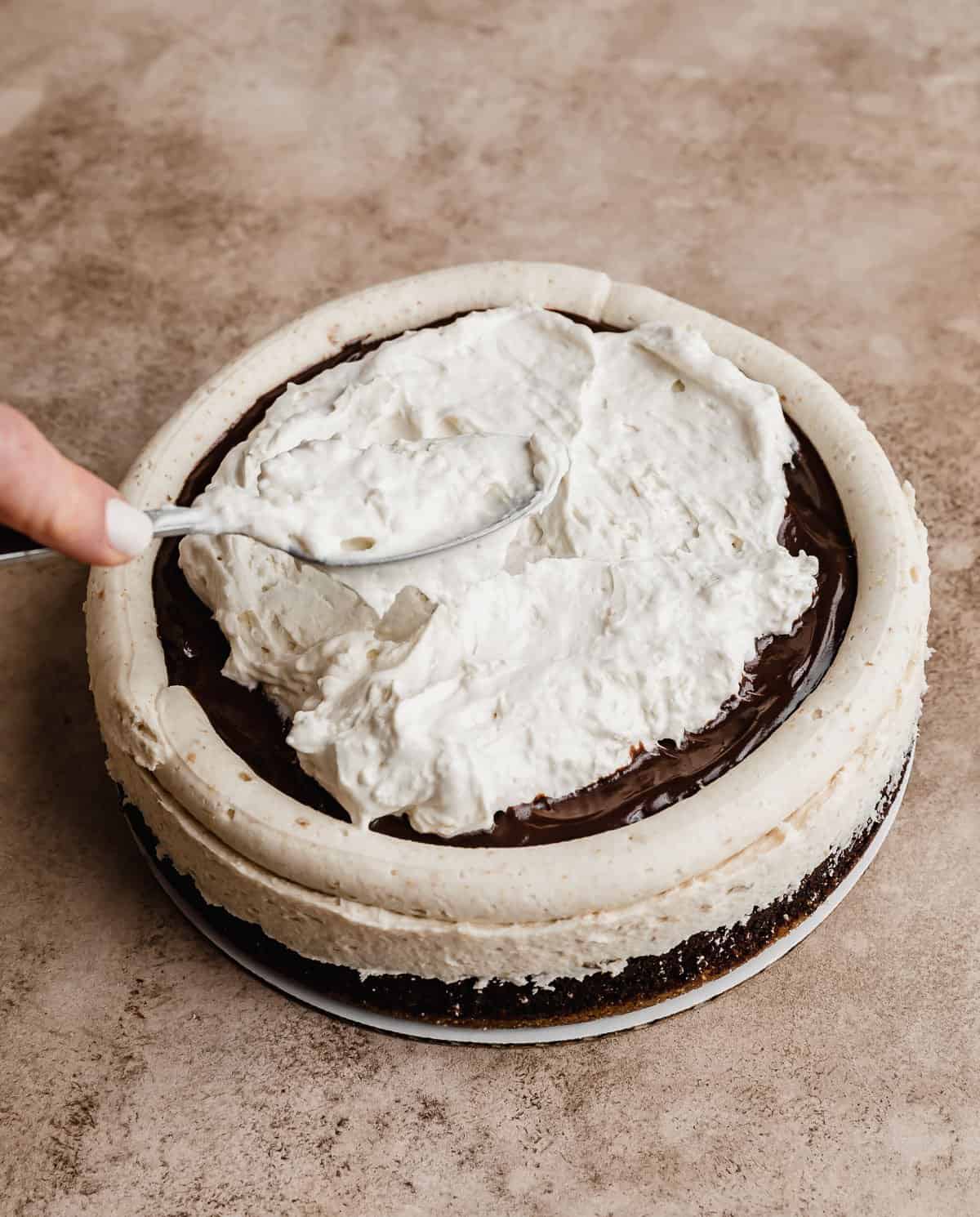 A fluffy marshmallow whipped cream being spread overtop a frosted S'mores Cake layer.