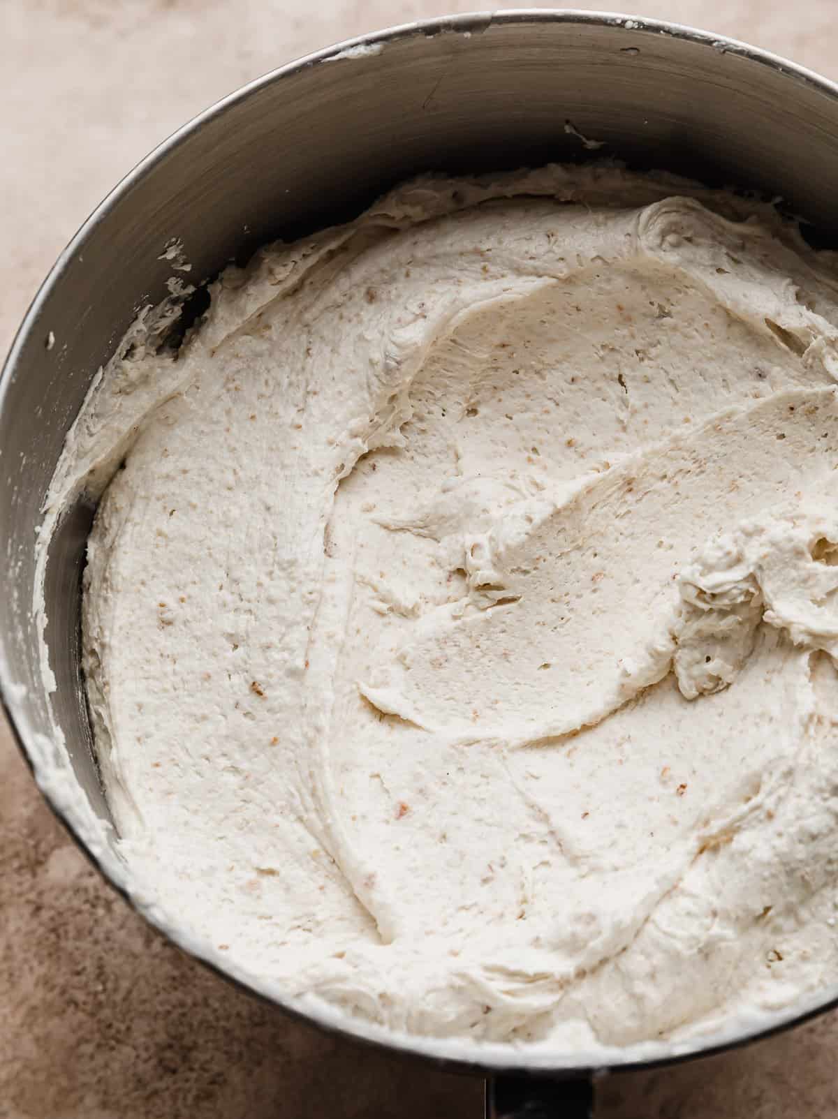 Graham Cracker crumbs mixed into white buttercream frosting in a metal bowl. 