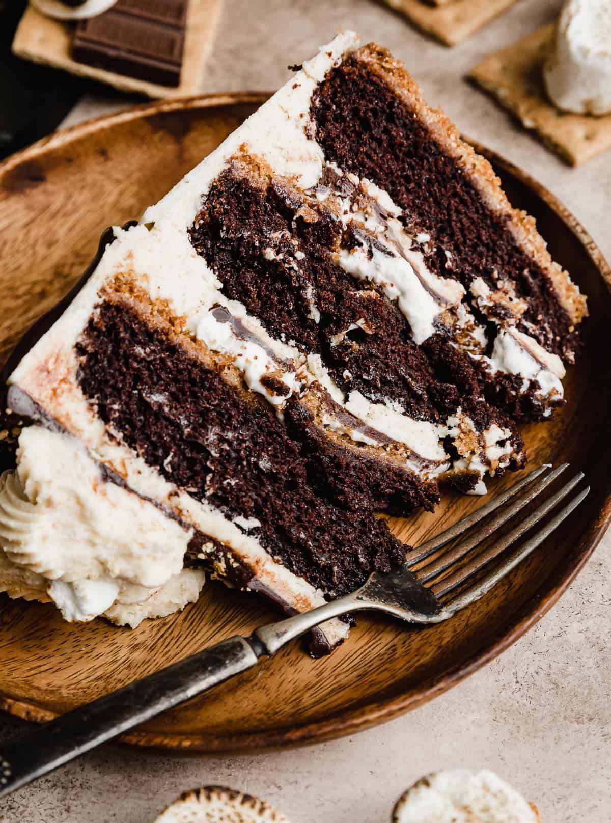 A s'mores cake slice on a brown plate with a fork next to the cake.