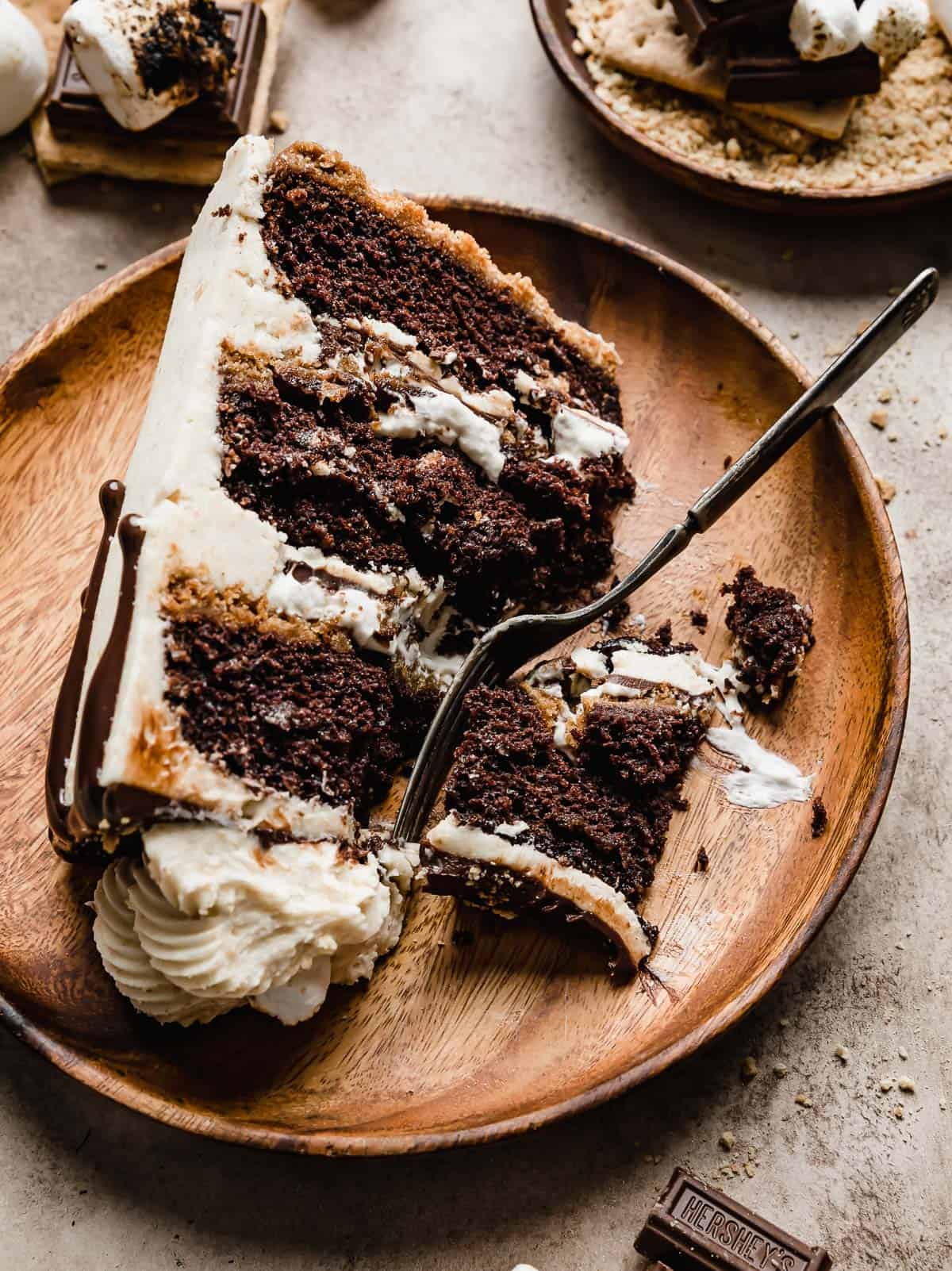 A slice of S'mores Cake on a brown wooden plate on a beige background.