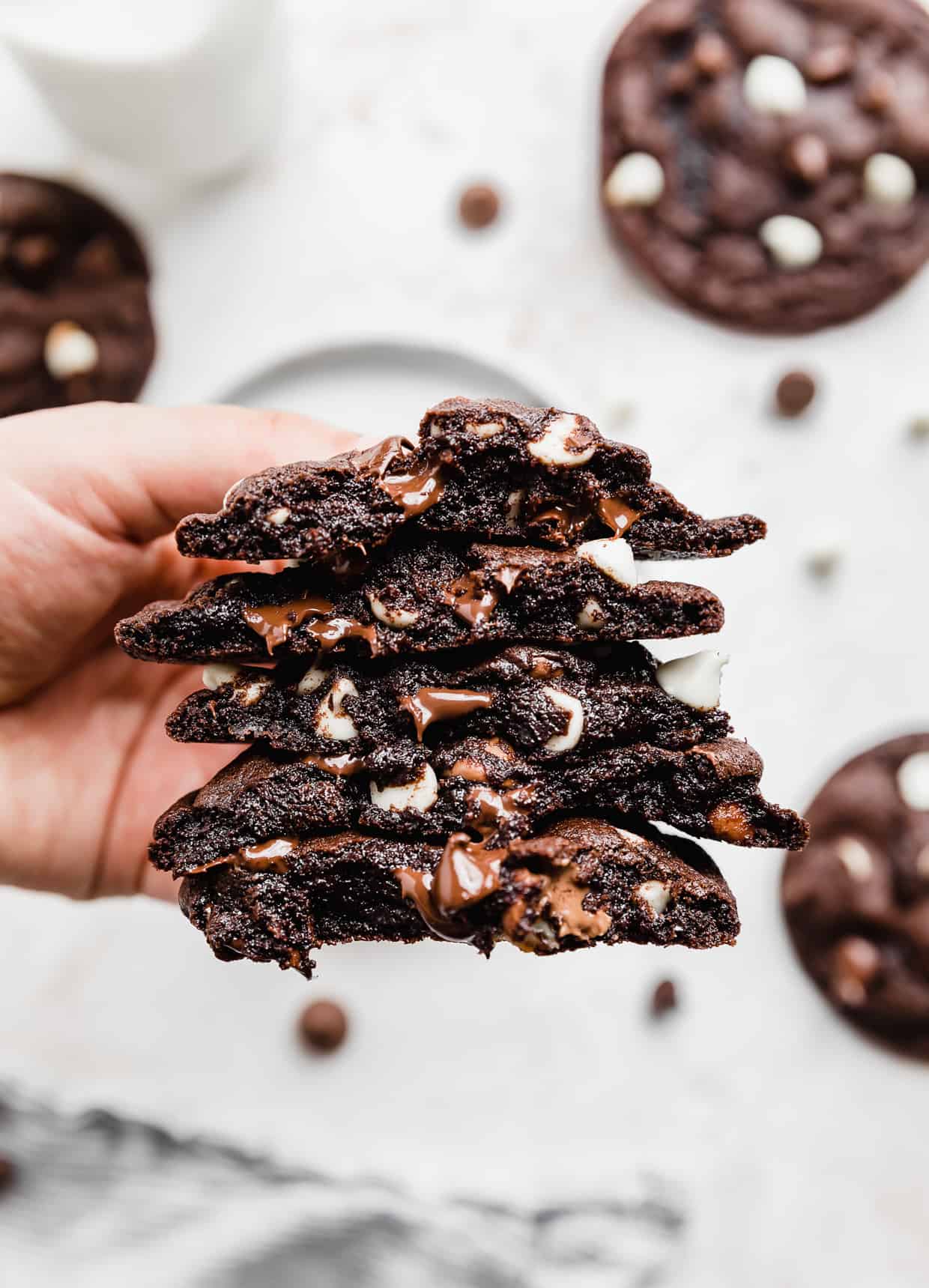 A hand holding a stack of Triple Chocolate Chip Cookies that have been broken in half. 