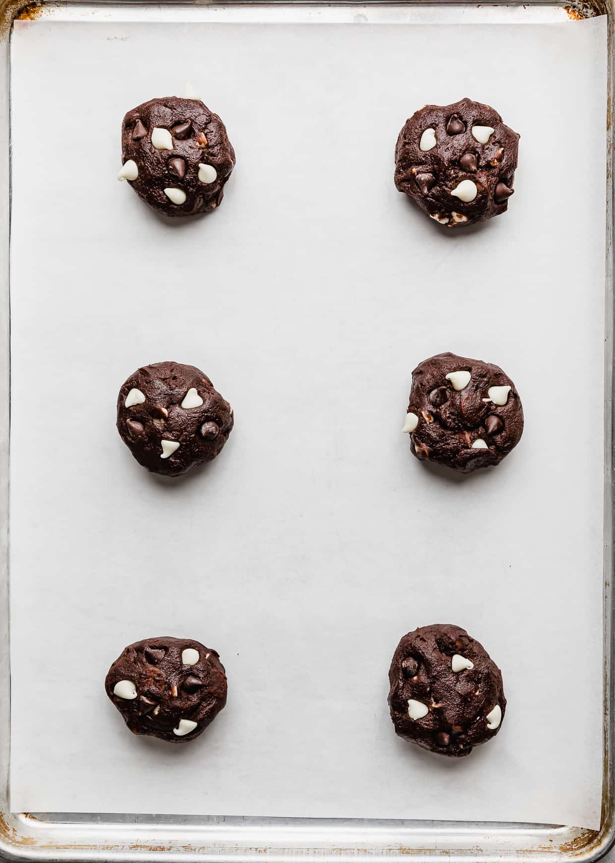 six Triple Chocolate Chip Cookie dough balls on a white parchment lined baking sheet.