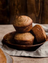 Three All Bran Muffins on a brown plate against a brown wooden background.