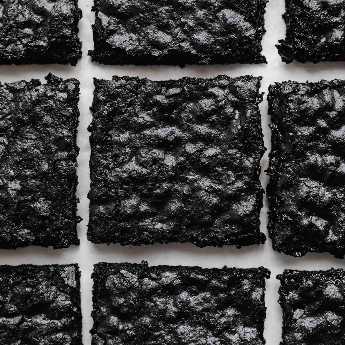 Crackly top Black Cocoa Brownies cut into squares on a white background.