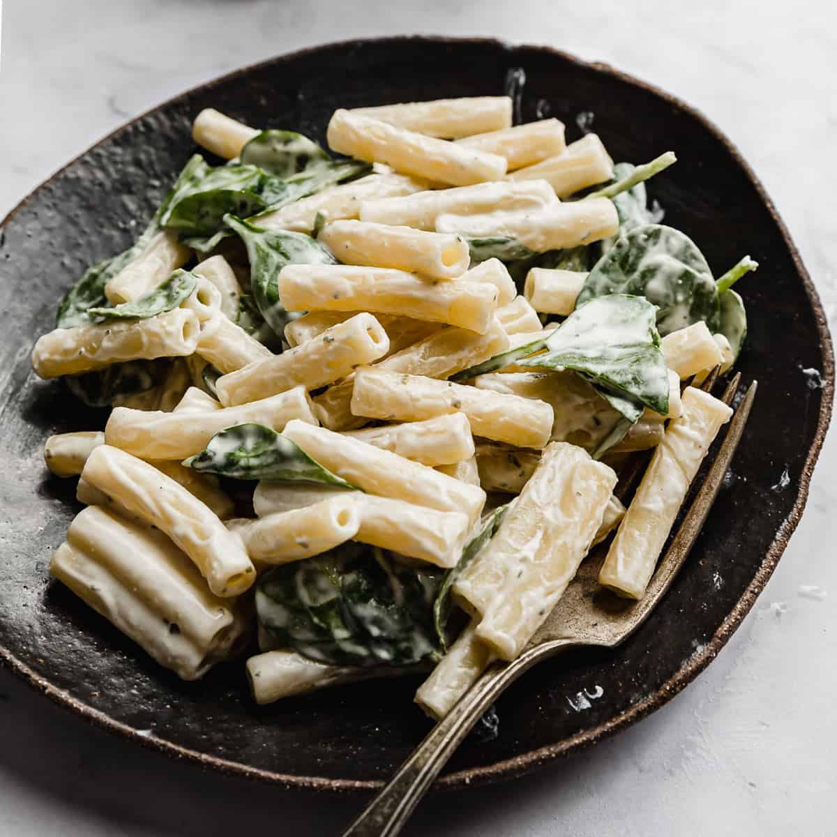 A black plate with creamy Boursin Pasta tossed with spinach.
