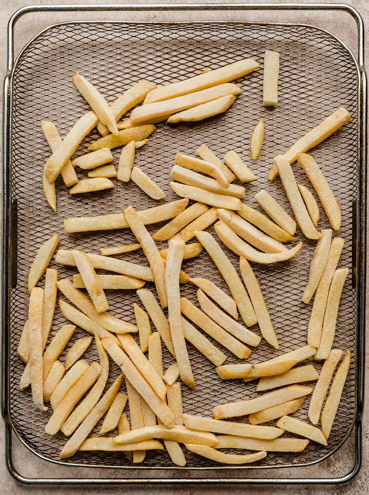 Frozen French fries on a metal air fryer basket.