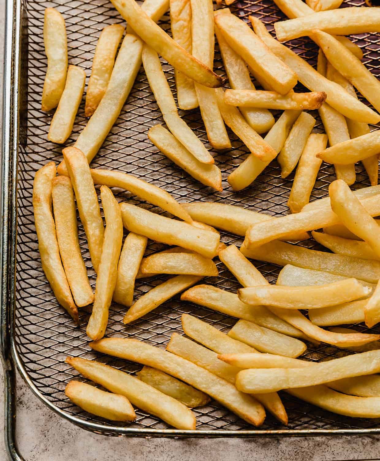 frozen French fries that were made in the air fryer, now golden and crispy on a metal air fryer basket.