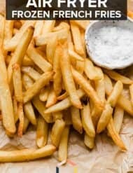 Frozen French fries in air fryer on a parchment paper with words "Air Fryer Frozen French Fries" written in white text.