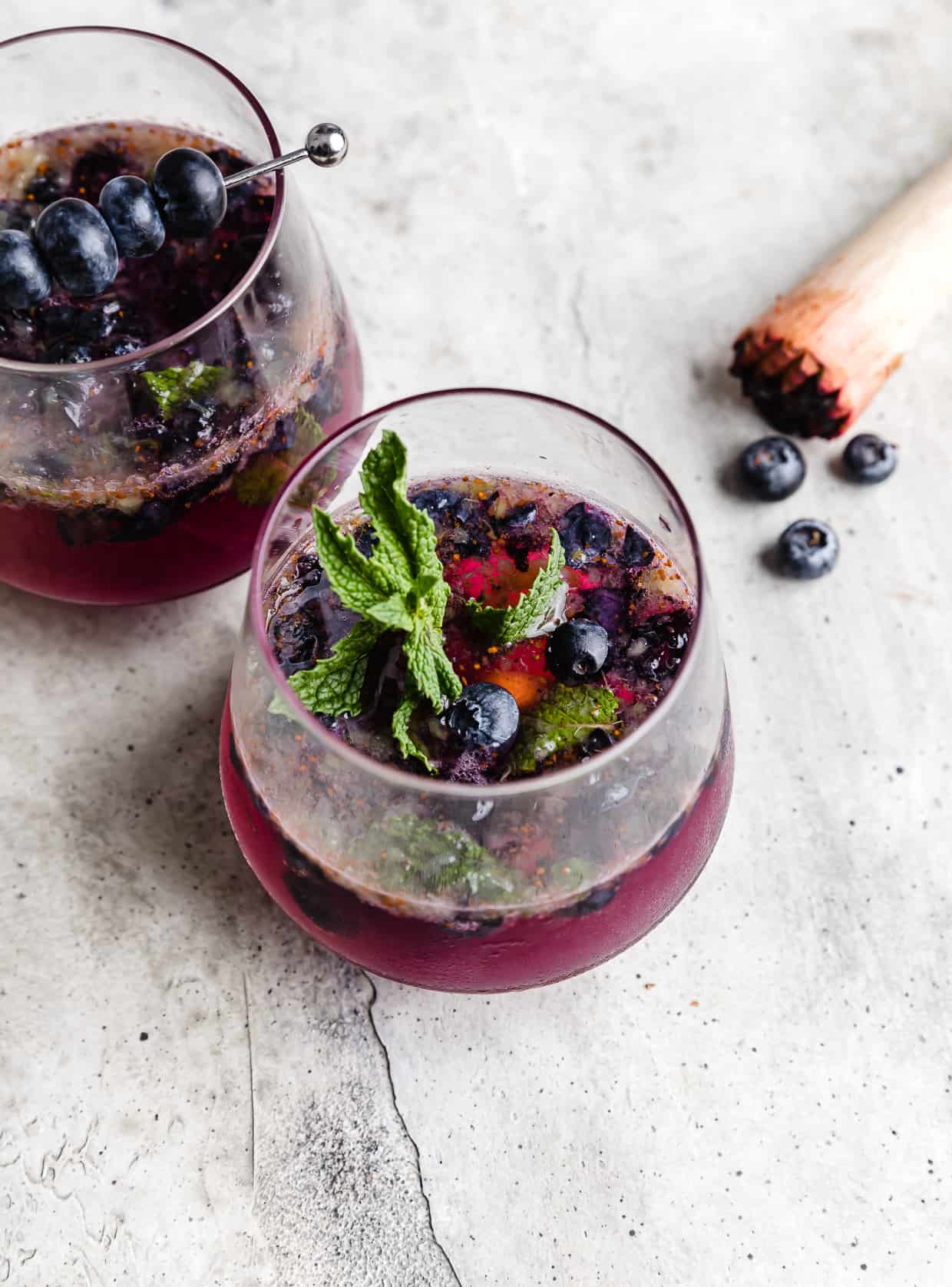 A glass filled halfway with a Blueberry Mint Mocktail and a mint sprig in the cup.