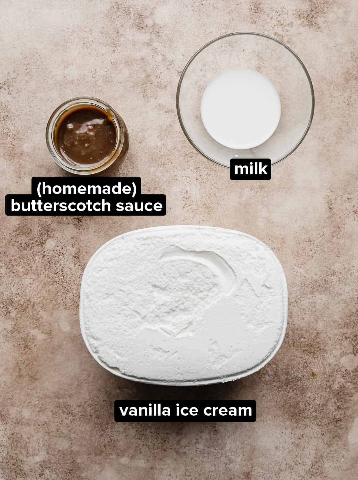 Butterscotch Milkshake ingredients: vanilla ice cream, milk, and butterscotch sauce on a tan textured background.