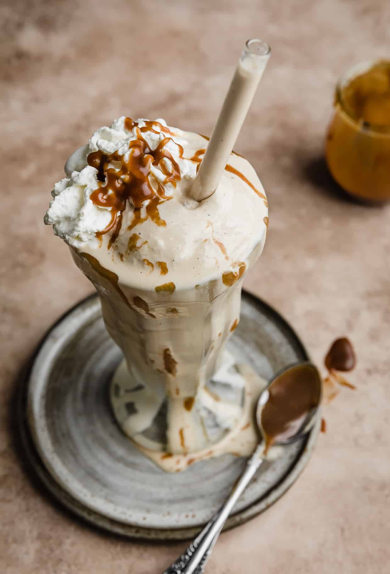 Butterscotch Milkshake in a glass jar with butterscotch sauce drizzled overtop and a straw in the top too.