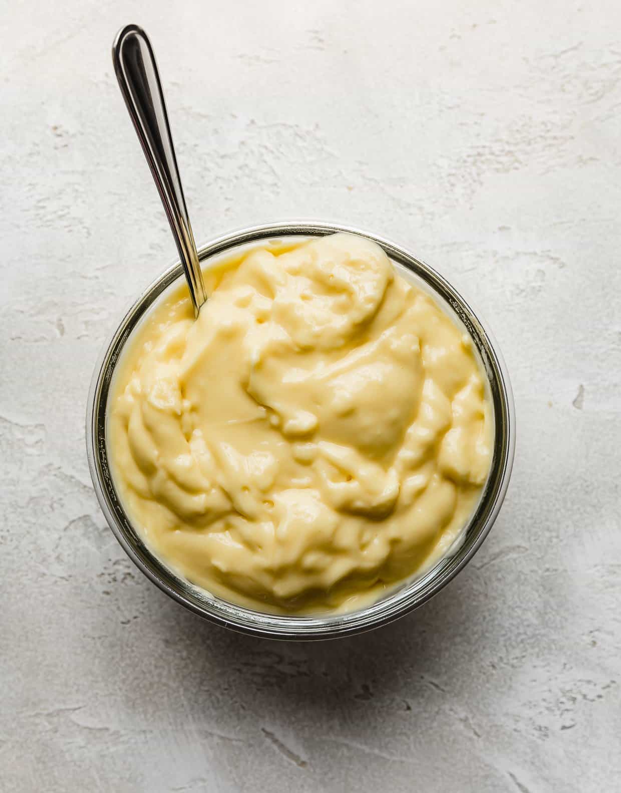 A yellow coconut pudding filling in a glass bowl on a light gray background.