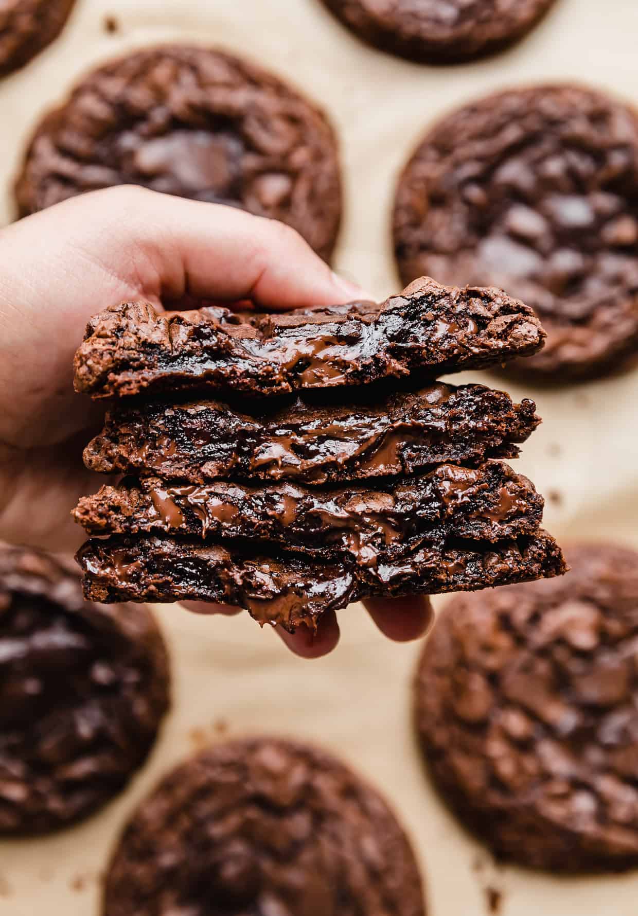 A hand holding four Crumbl Brownie Batter Cookies that have been cut in half, showcasing the inner gooeyness.