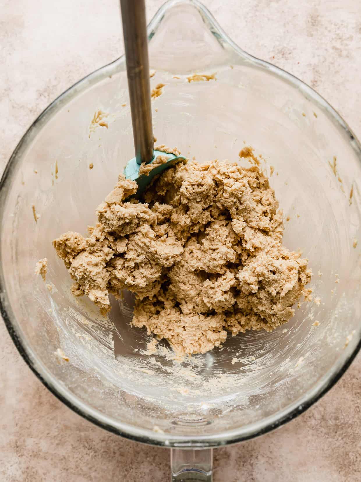 Peanut butter cookie dough in a glass mixing bowl on a light brown textured background.