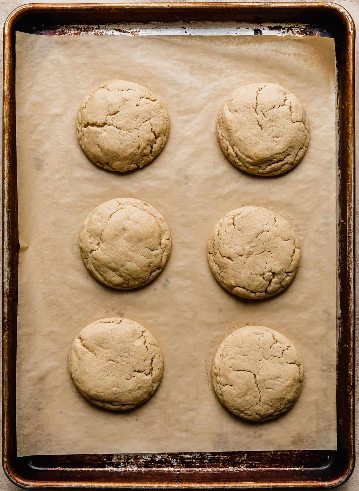 Six peanut butter cookies on a tan parchment paper lined baking sheet.