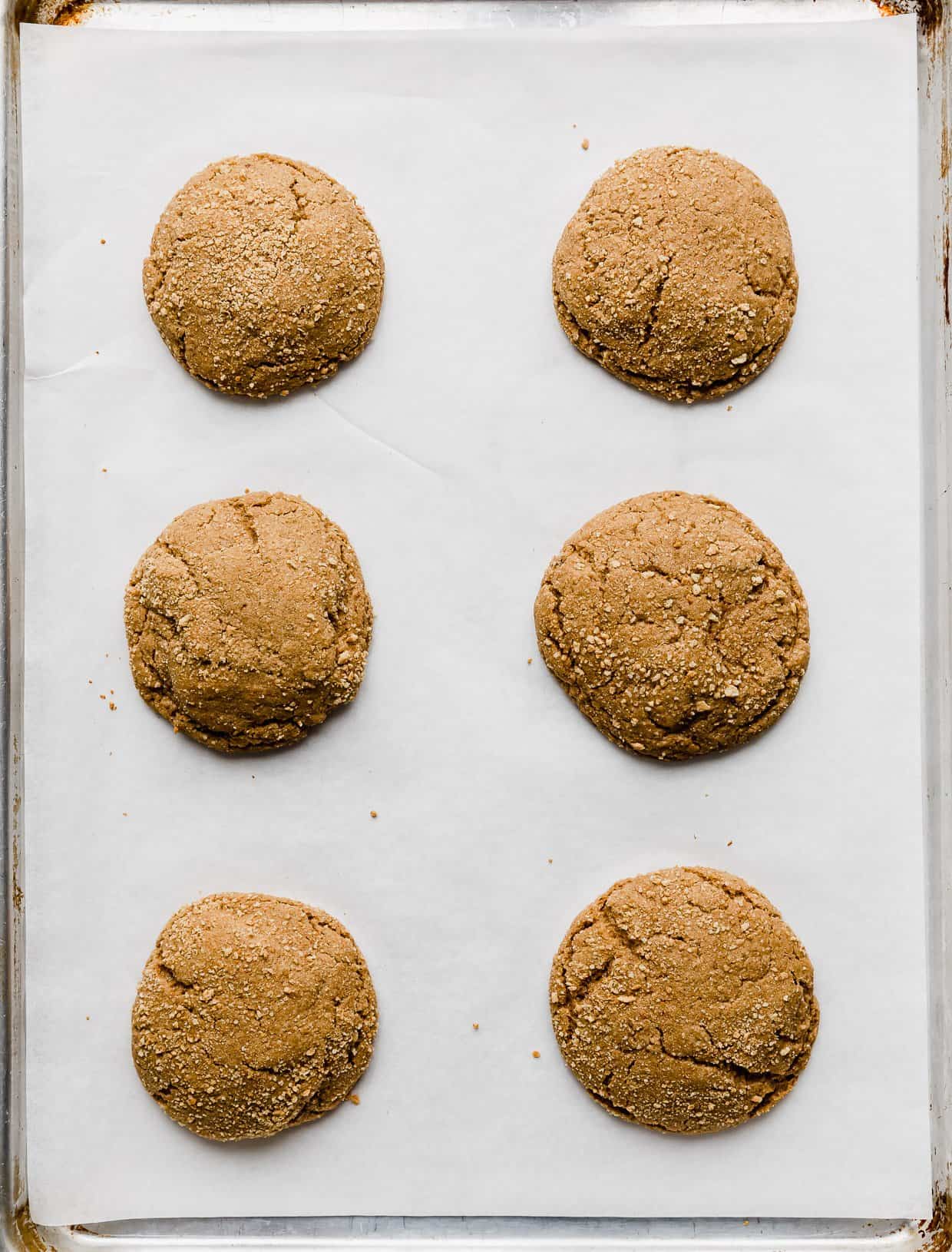 Six baked dark brown sugar graham cracker cookies on a white parchment lined baking sheet.