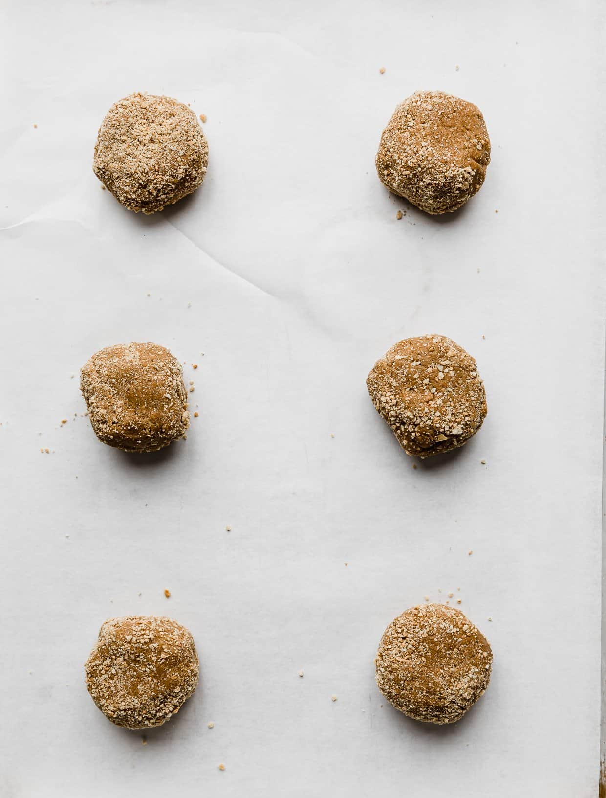 Six Crumbl New York Cheesecake Cookie dough balls on a white parchment paper.