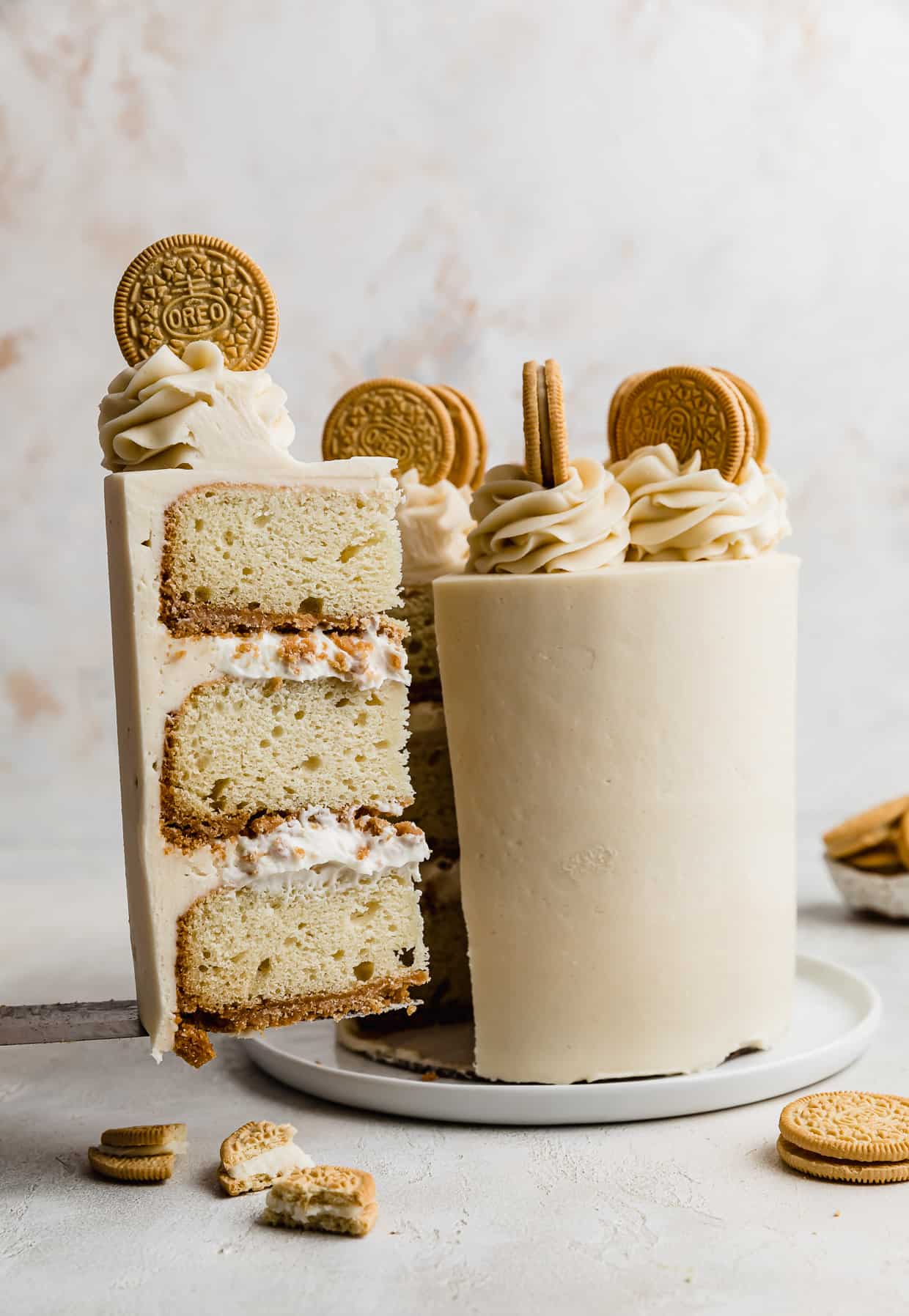 A slice of Golden Oreo Cake balancing on a knife infant of a decorated Golden Oreo Cake.