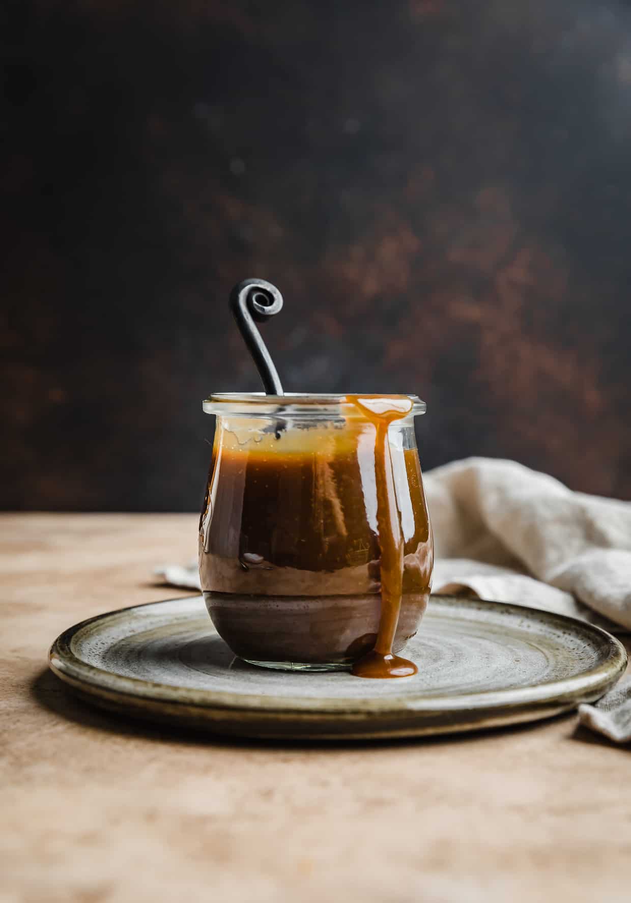 Homemade butterscotch recipe in a glass jar against a brown background.