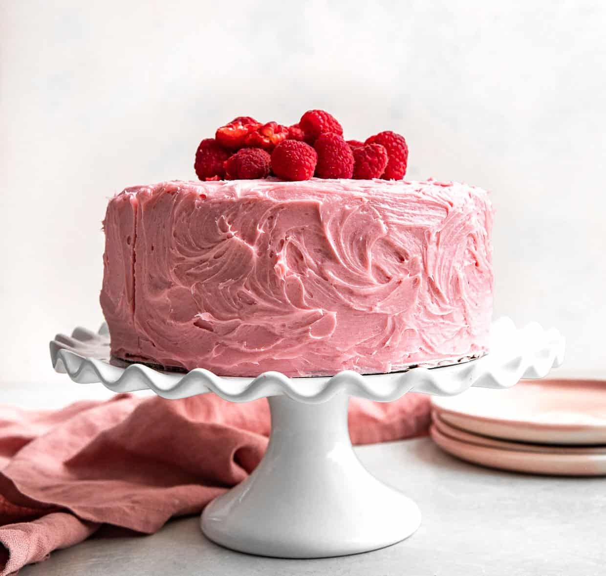A two layer Lemon Raspberry Cake frosted with pink frosting on a white cake stand.