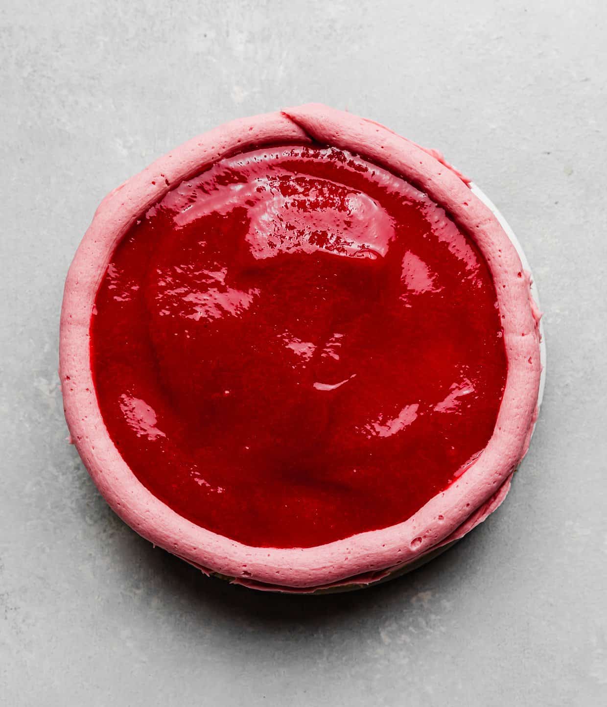 Overhead photo of a raspberry sauce overtop a round cake layer.