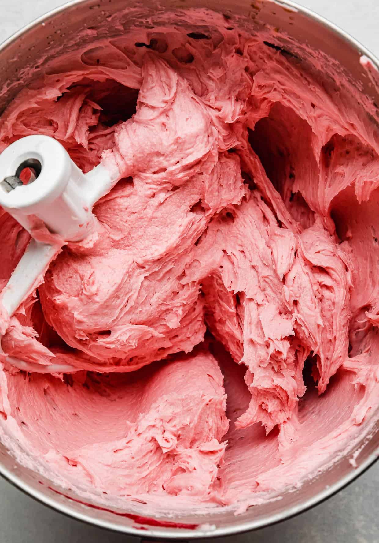 A pink colored raspberry buttercream in a metal mixing bowl.