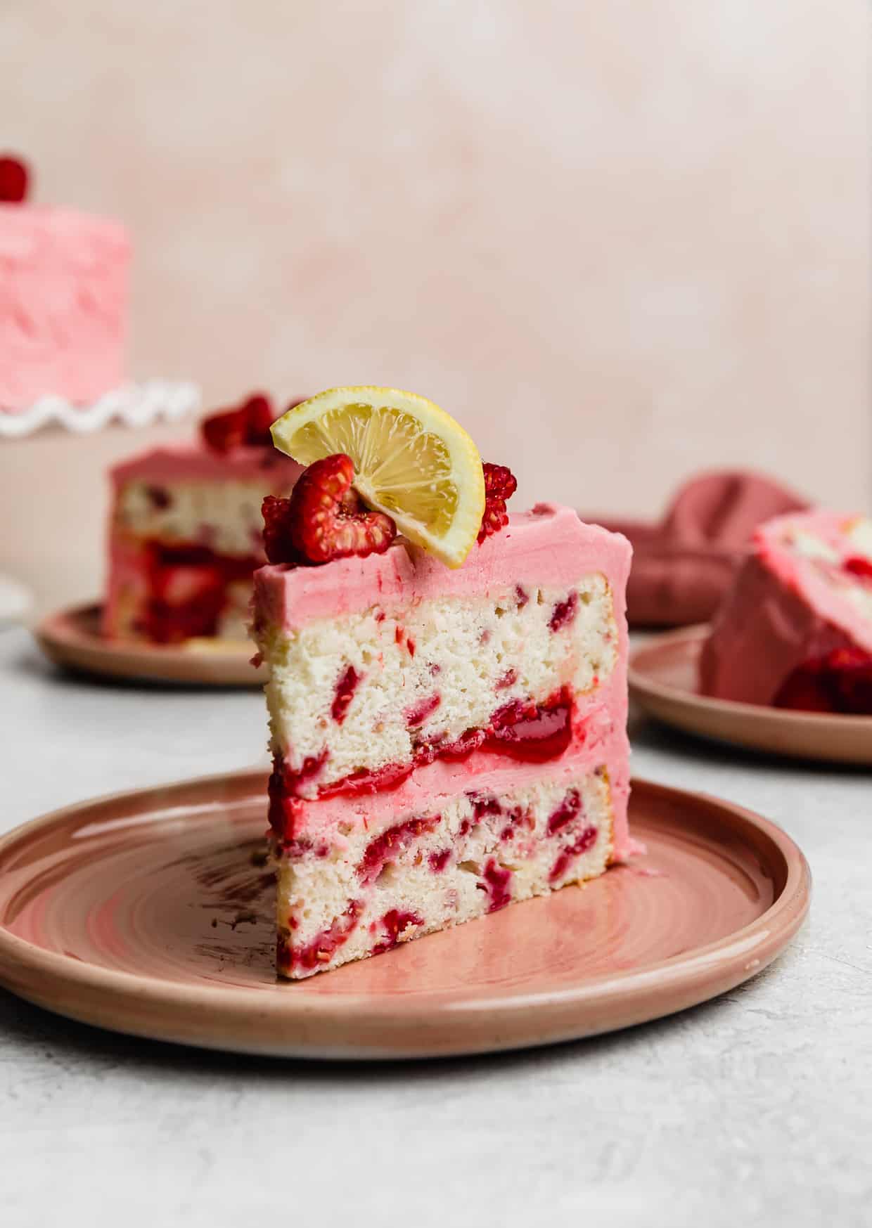 A slice of Lemon Raspberry Cake on a pink plate against a light pink background.