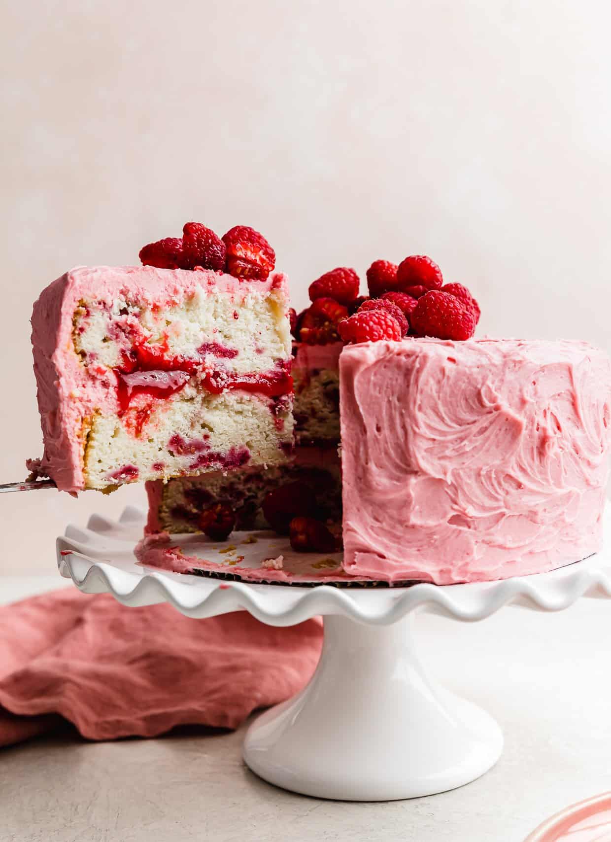 A slice of fresh Lemon Raspberry layer cake on a knife being lifted from the full cake.