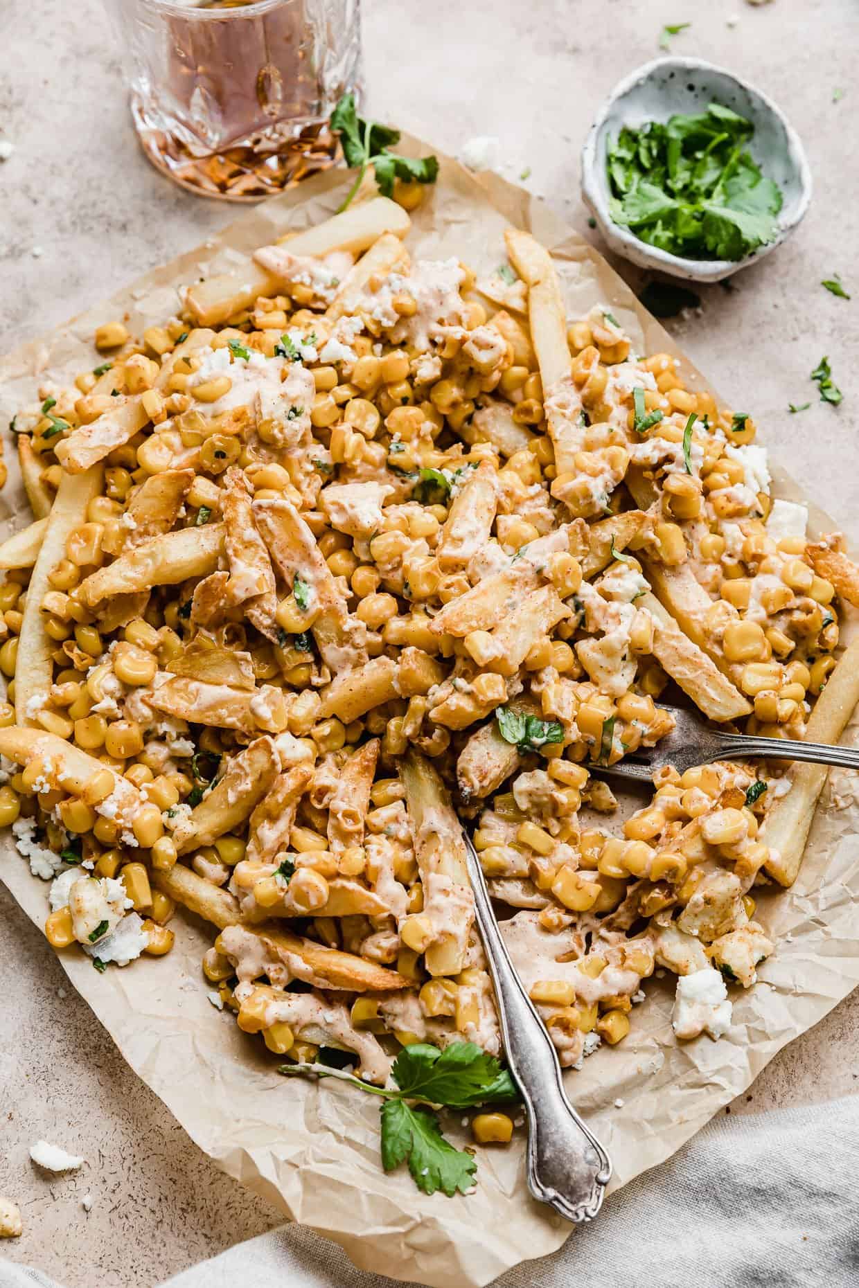 Fries topped with a Mexican Street Corn mixture, cheese, and cilantro on a parchment paper.