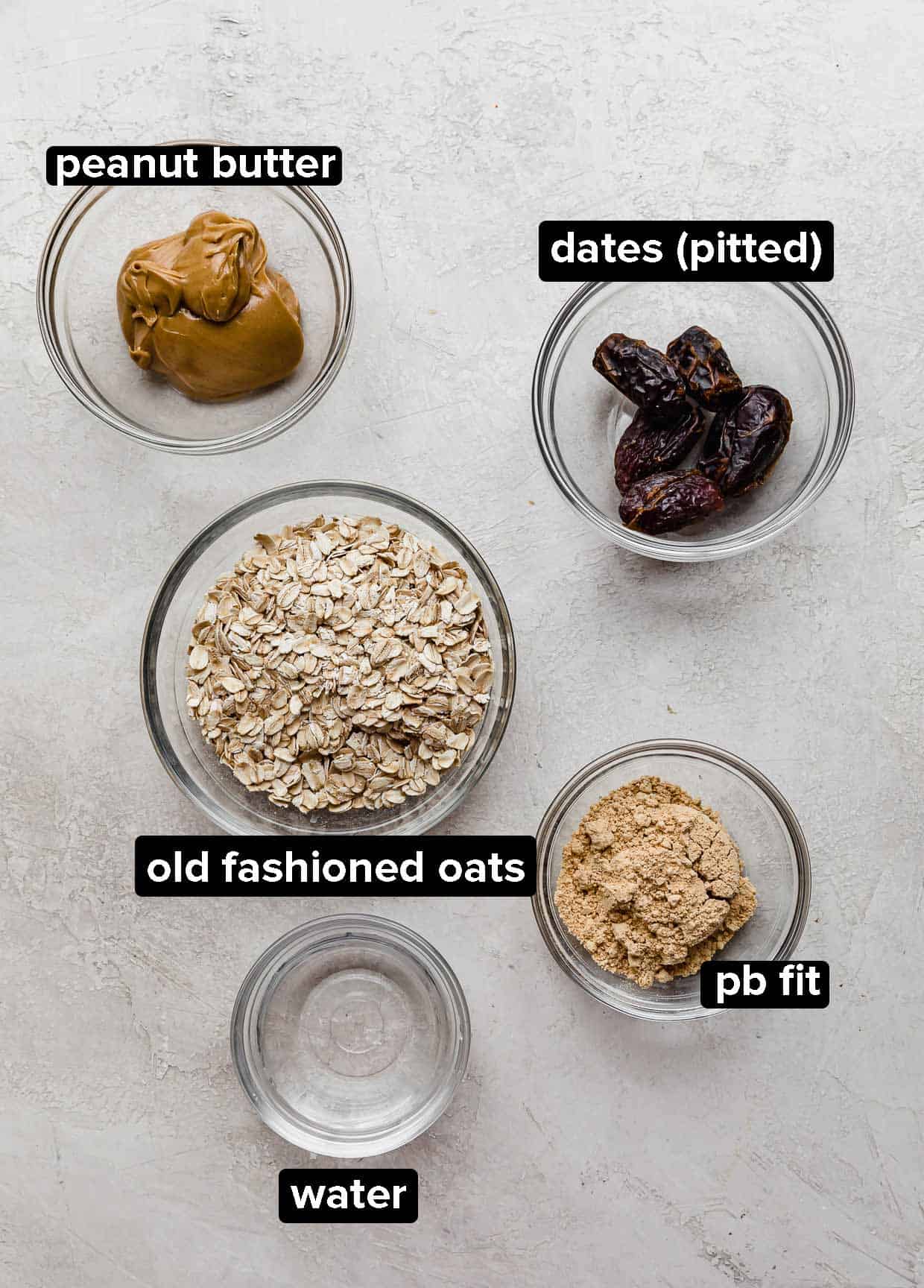 Peanut Butter Bliss Balls ingredients portioned into glass bowls on a light gray background.