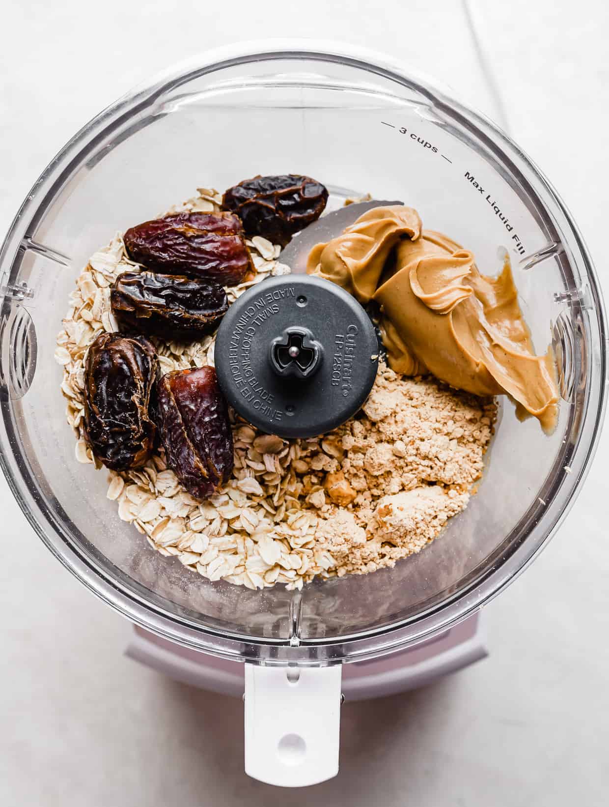 A food process with dates, peanut butter, oats, and powdered peanut butter in it.