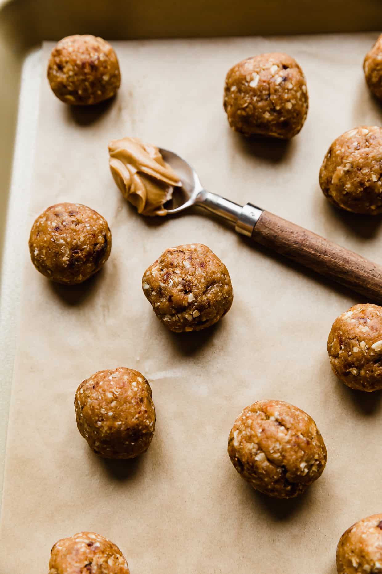Small round Peanut Butter Bliss Balls on a tan parchment paper with a spoon of peanut butter in the background. 
