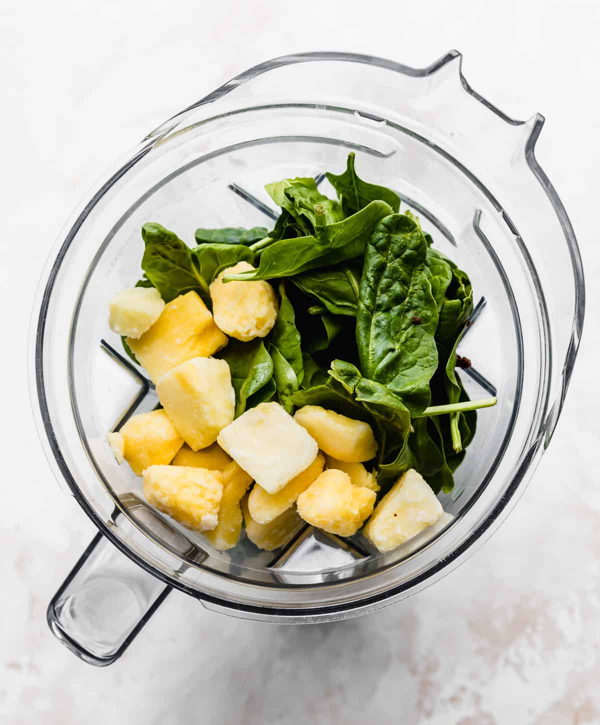 Overhead photo of a blender filled with fresh spinach leaves and frozen pineapple chunks.