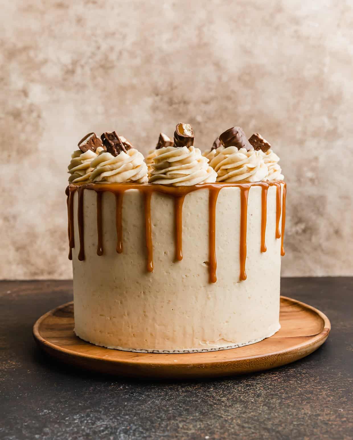 A Twix Cake on a wooden plate against a cream textured background. 