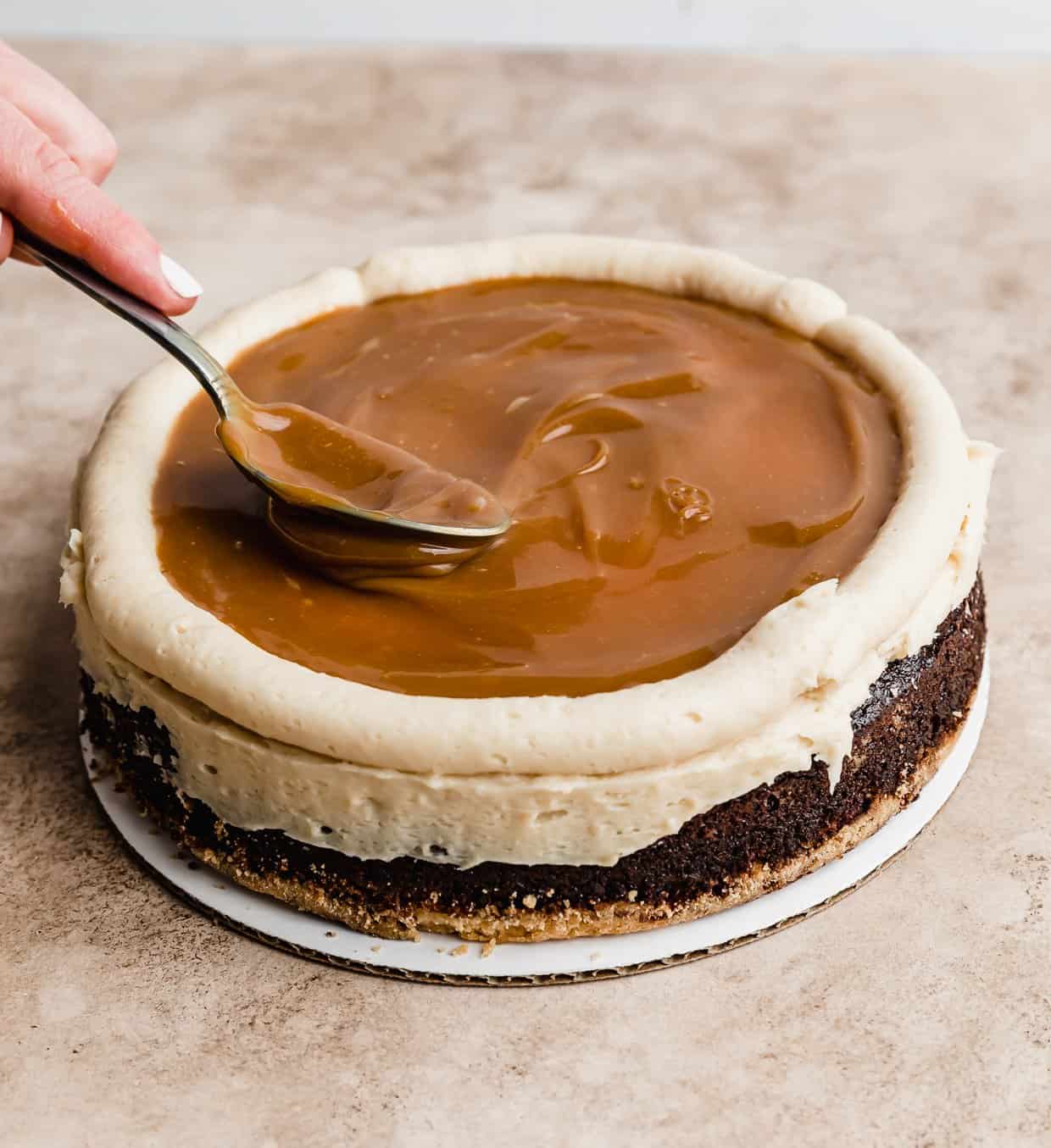 A spoon spreading caramel overtop a shortbread buttercream frosted chocolate cake layer.