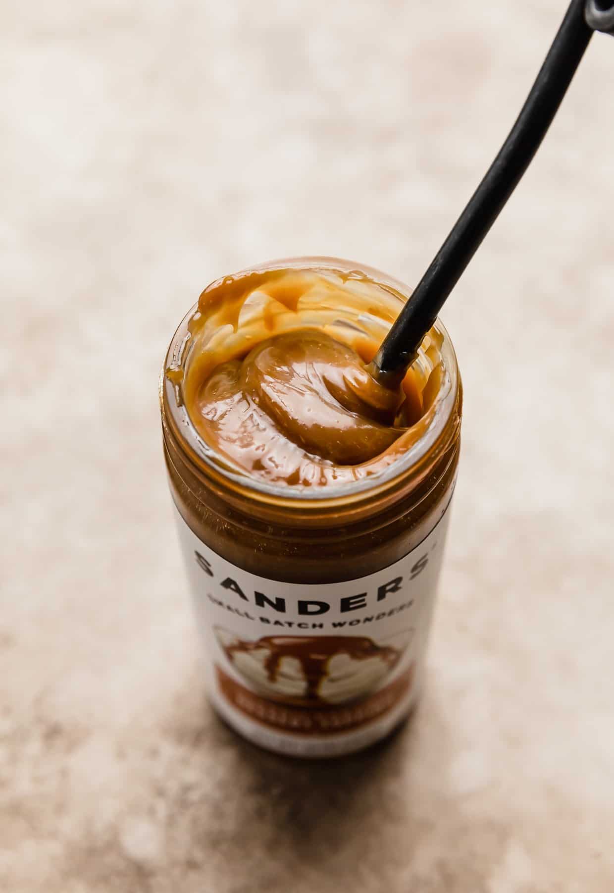 A jar of sanders caramel with a spoon in the caramel.