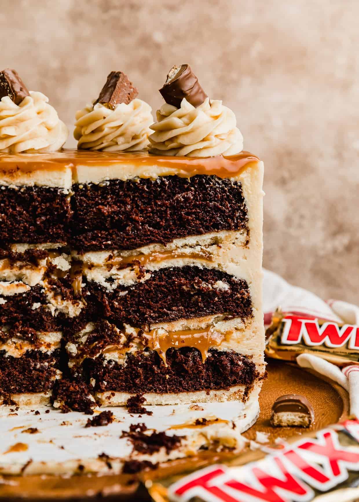A three layer Twix cake with chocolate layers baked on a shortbread crust with caramel oozing out between each layer. 
