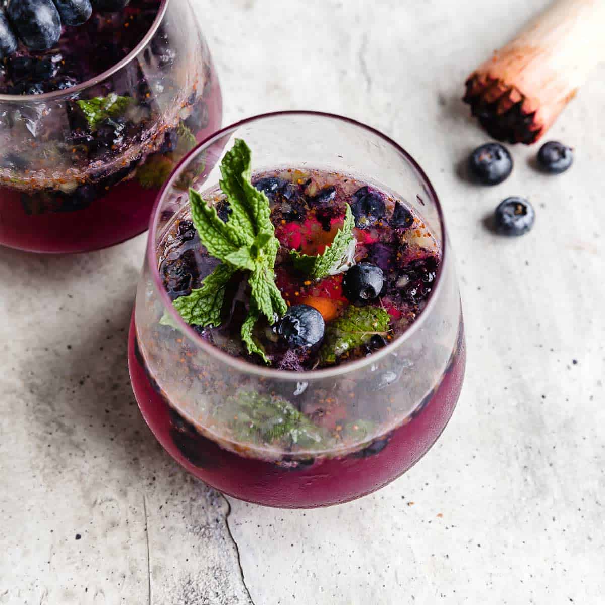 A glass cup on a gray background filled with a blueberry mojito mocktail.