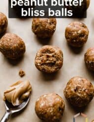 Small healthy peanut butter loaded bliss balls on a tan background with the words "Peanut Butter Bliss Balls" written in white text over the photo.