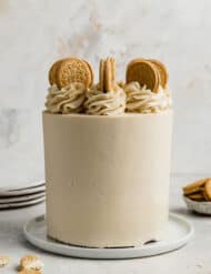 A three layer Golden Oreo Cake on a white plate against a white textured background.