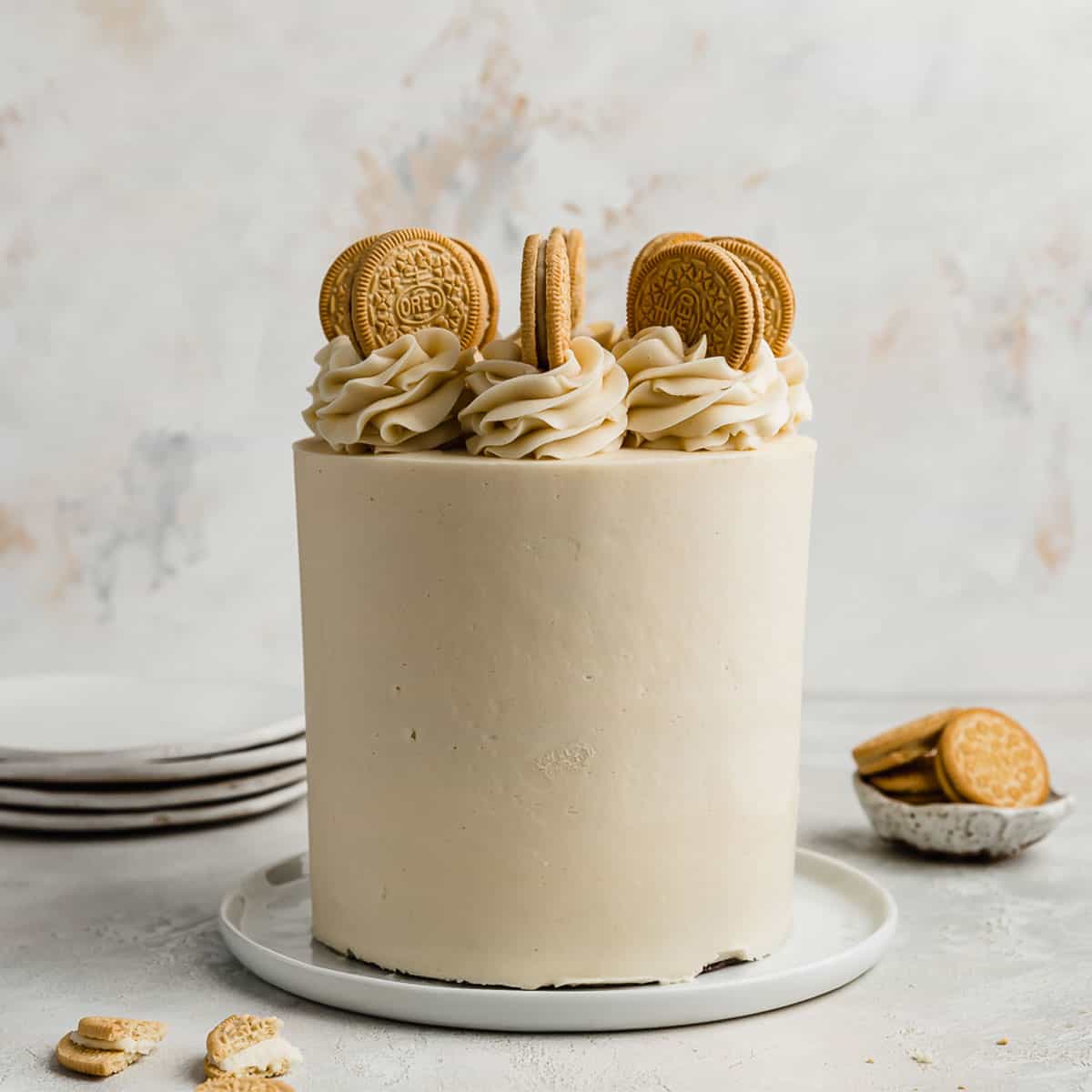 A three layer Golden Oreo Cake on a white plate against a white textured background.