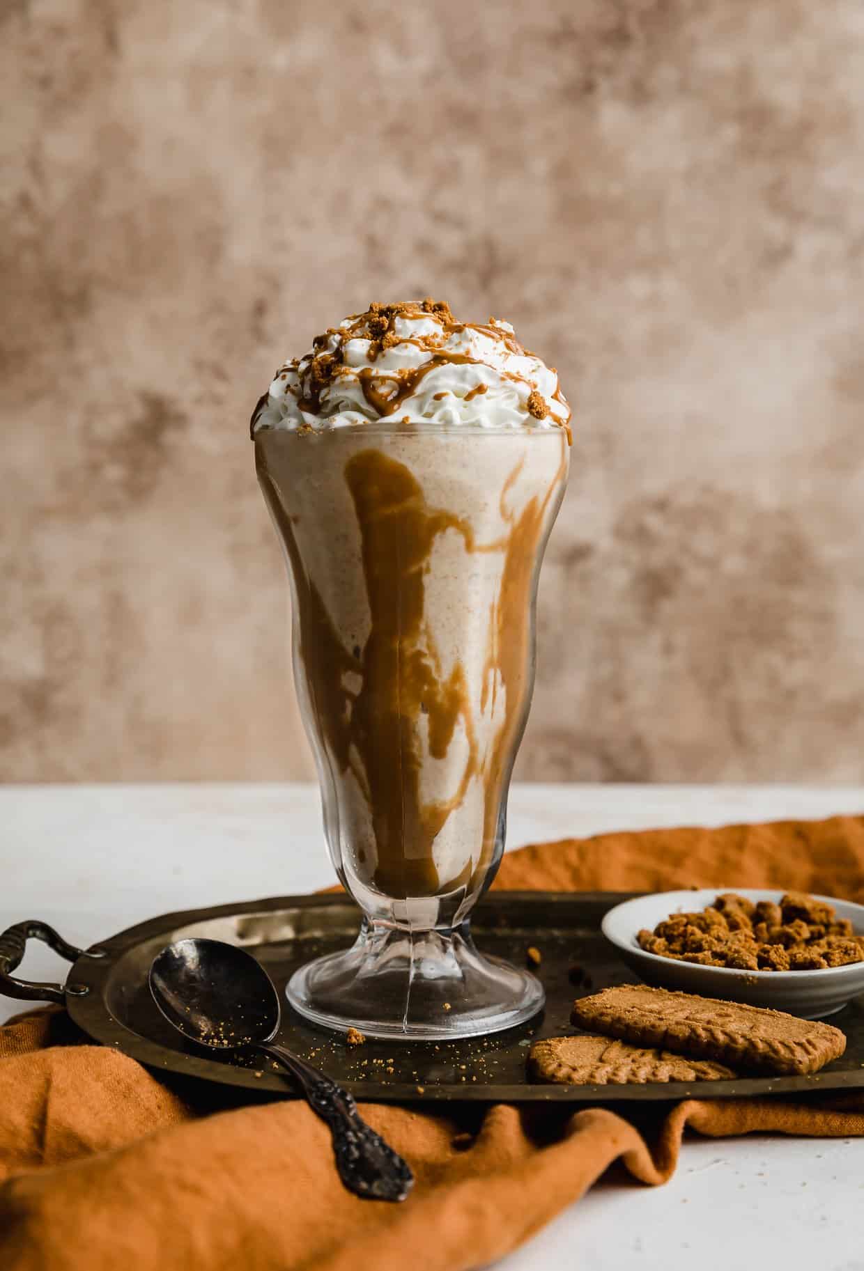 A Biscoff Milkshake in a glass cup against a light brown background.