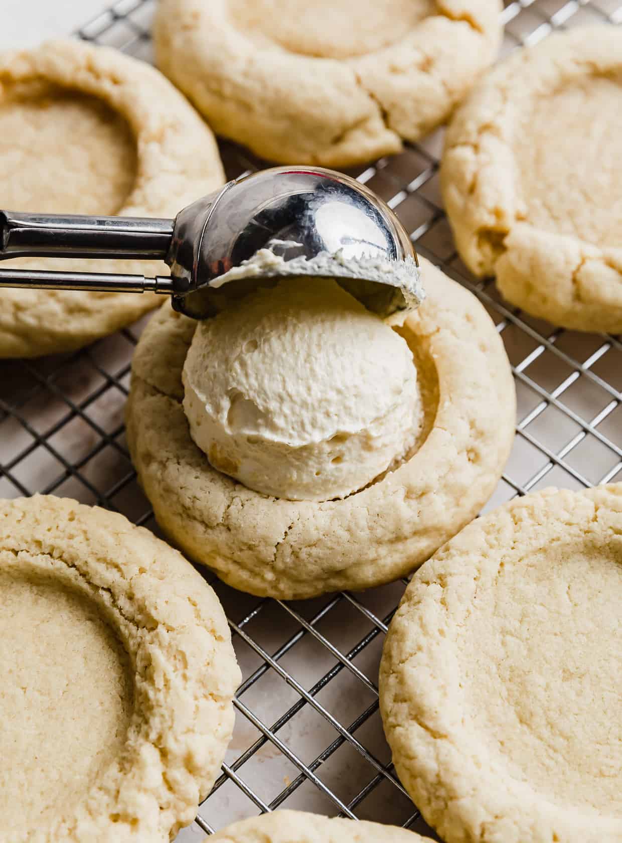 A cookie scoop portioning a light yellow colored cream on top of a sugar cookie.