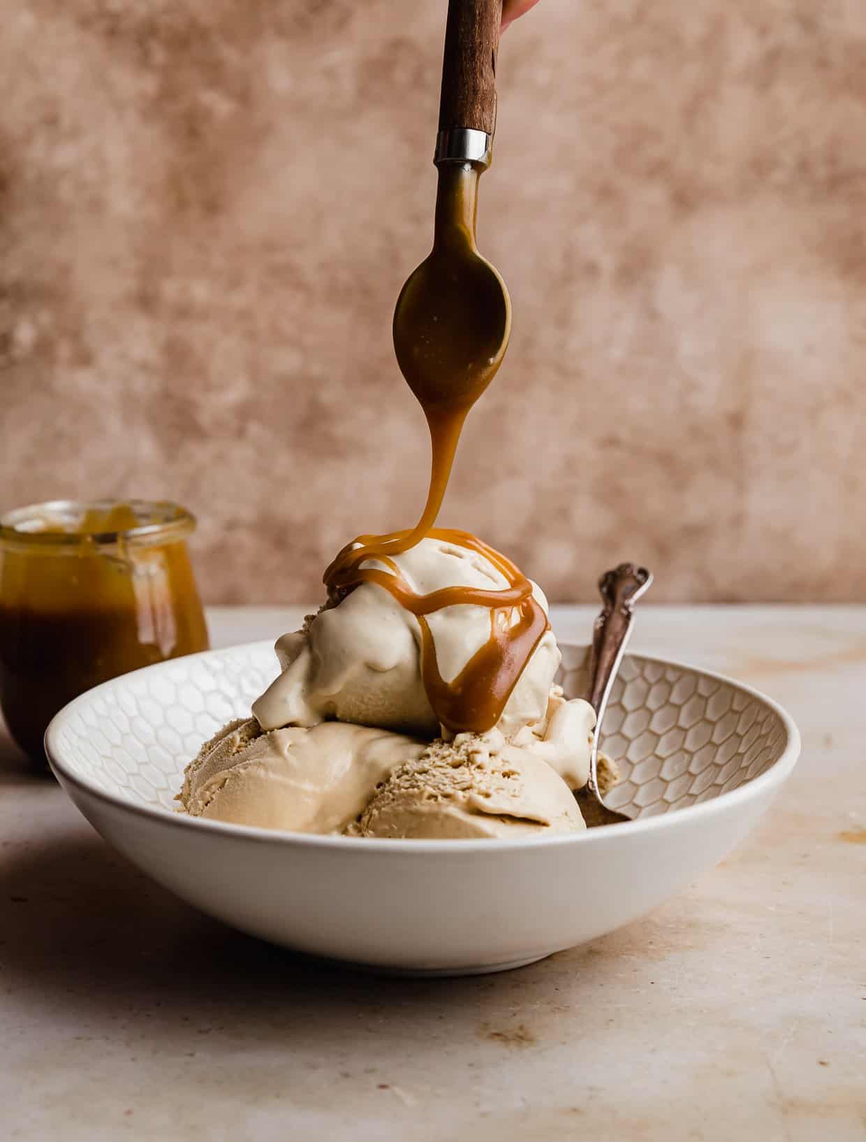 Butterscotch Ice Cream in a white bowl with a spoon drizzling homemade Butterscotch sauce overtop.